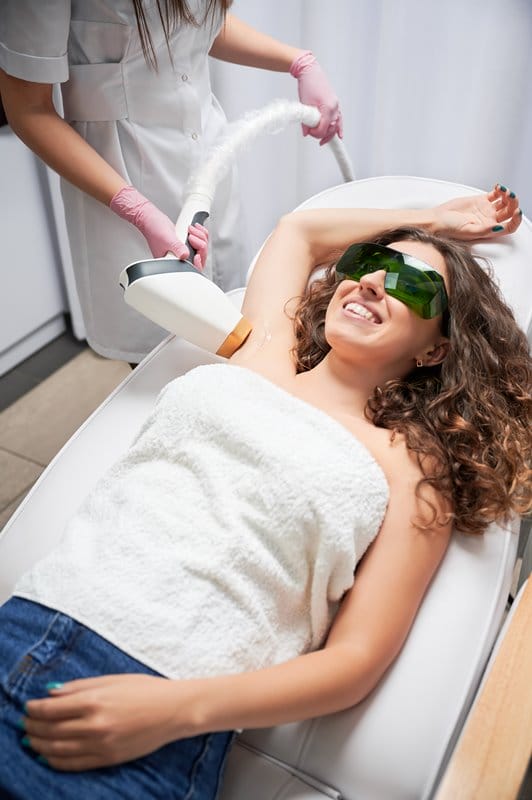 Joyful woman receiving underarm laser hair removal treatment.